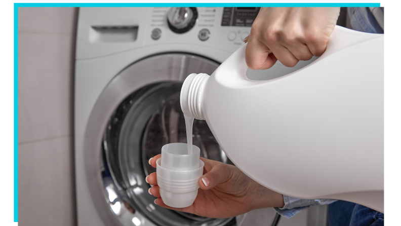 A pair of hands pouring detergent into a cup for a washing machine.