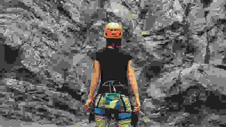 Young woman wearing in climbing equipment standing in front of a stone rock outdoor and preparing to climb, rear view