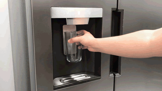 Person placing drinking glass under water and ice dispenser on fridge.