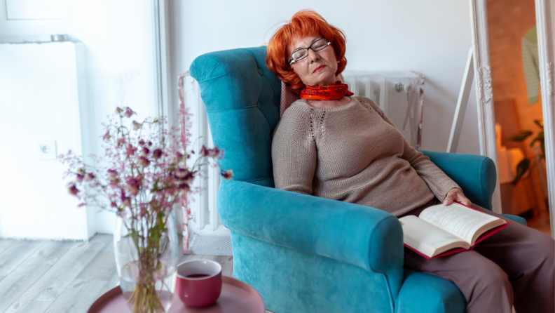 A person sleeps in a recliner chair with a book in their lap.