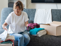Person sorting folded clothes in order to donate them while sitting on couch.