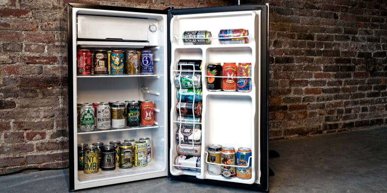 The Igloo 3.2-Cu.-Ft. Platinum Fridge sitting in front of a brick wall with its door open, showcasing a bunch of different kinds of beer.