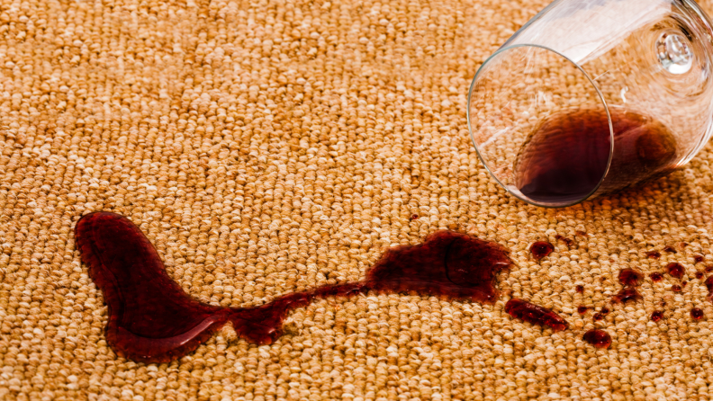 A glass of red wine spilling onto carpet.
