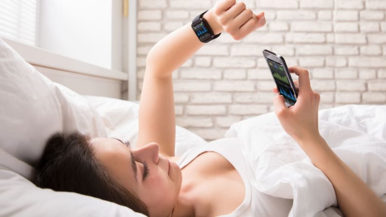 a person lies on their back looking at their phone and wearable in bed