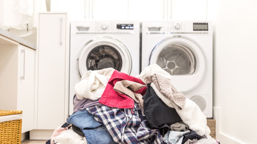 Pile of dirty laundry in front of a washer and dryer set