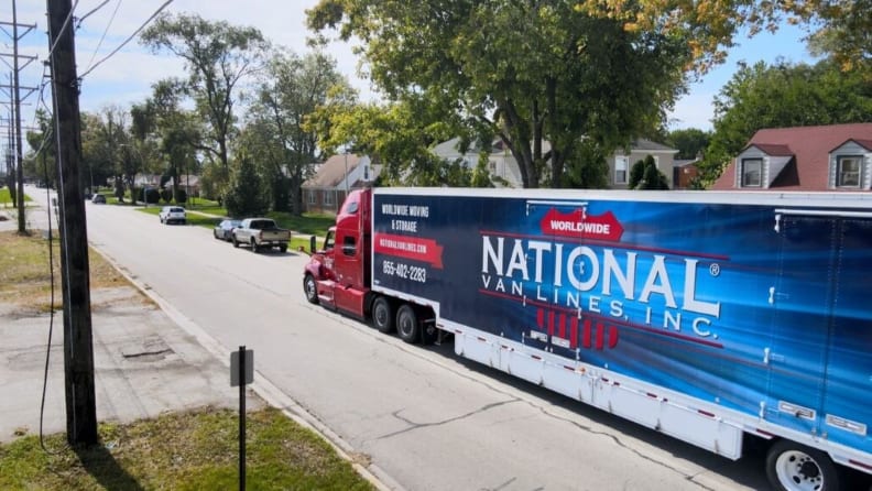A blue moving truck parked on a street in front of a house