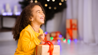 A young girl holds a wrapped present and laughs