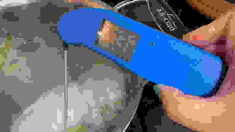 A person is poking a Thermapen ONE digital meat thermometer in Blue into a piece of poached chicken in a large pot.