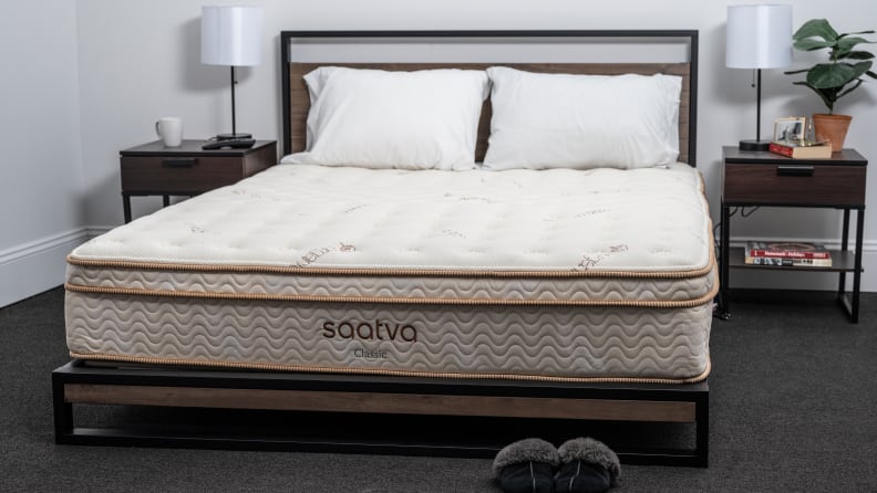 the saatva mattress on a wood and metal bed frame with pillows