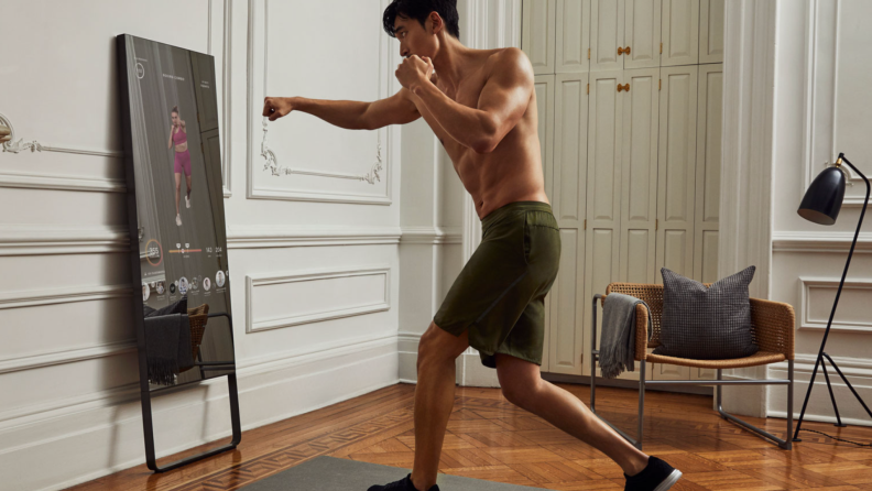 Person with extended fist in front of the lululemon Studio Mirror on top in yoga mat.