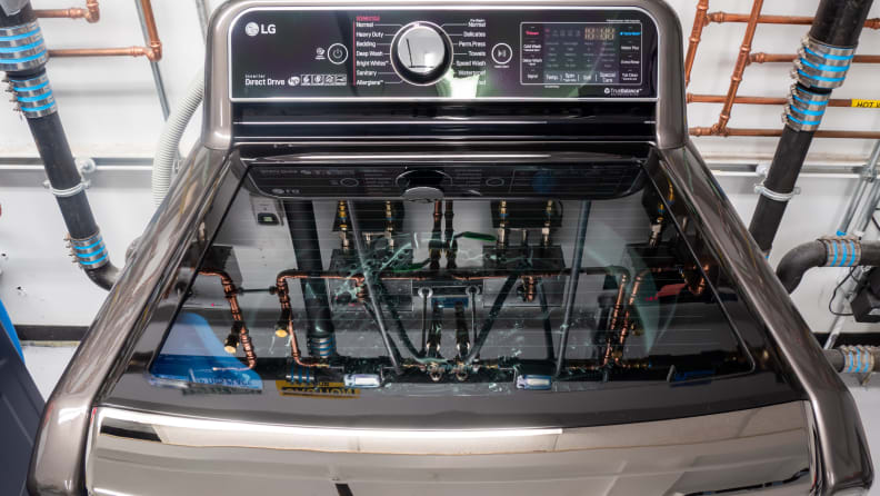 A close-up of an LG top-loader in our testing labs. Behind the appliance and in the reflection on its translucent lid you can see a network of pipes we use to regulate water temperature and flow.