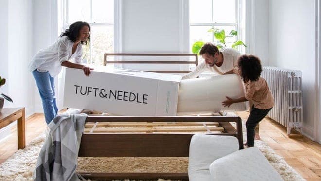Group of friends assembling mattress in bed frame.
