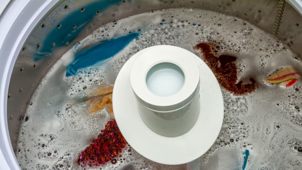 Basin of washing machine with an agitator pole. Basin is filled with soapy water and linens.