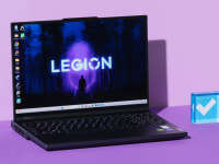 Black Lenovo Legion Pro 5i Gen 8 gaming laptop opened with desktop screensaver on screen next to blue acrylic paperweight in the middle of purple setting.