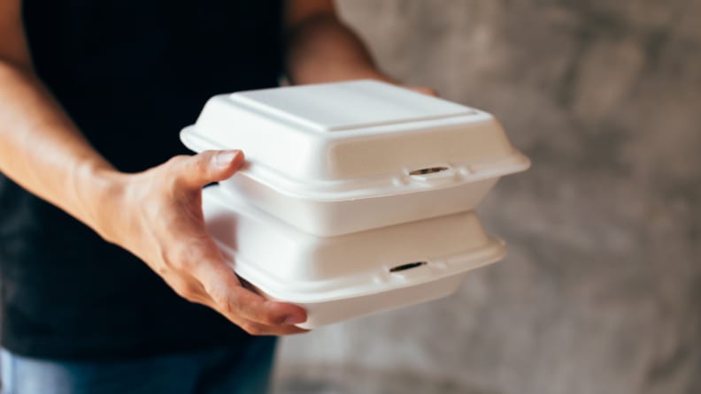 Person carrying two takeout boxes stacked on top of each other with both hands.