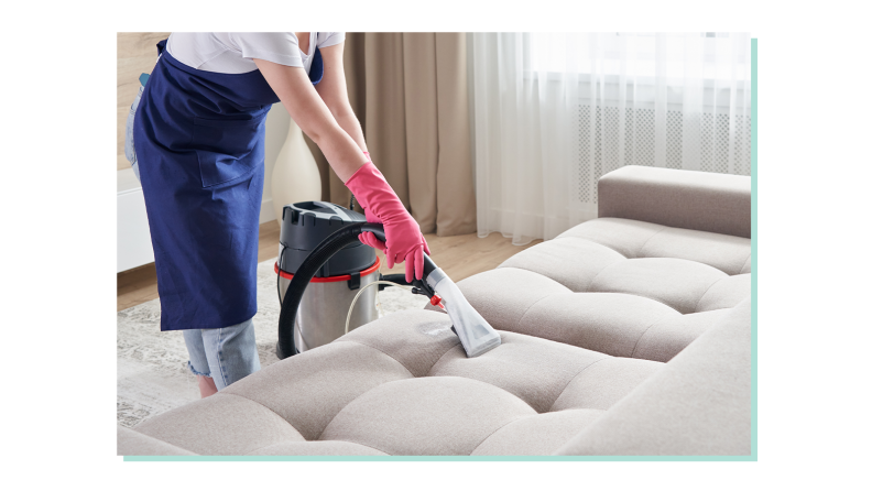 Person wearing gloves and apron to complete indoor cleaning on couch.