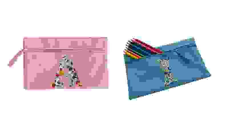 On right, pink pencil pouch with the letter "A" on the front. On right, blue "I" lettered pencil case with multiple colored pencils sticking out.