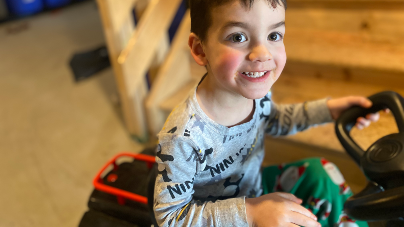 A smiling young boy sitting on a ride-on toy.