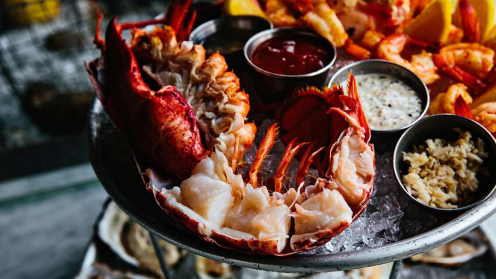 On a tray filled with crushed ice, there lies a half lobster and three little bowls of dipping sauces.