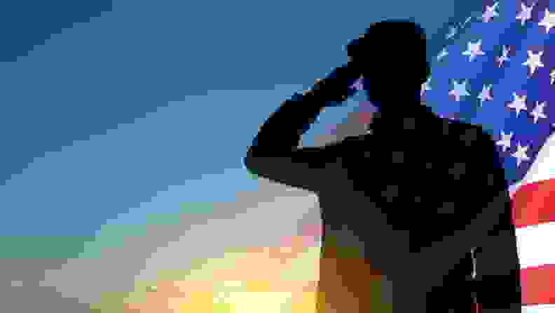 Silhouette of a soldier saluting in front of a U.S. flag and a blue sky and sunrise.