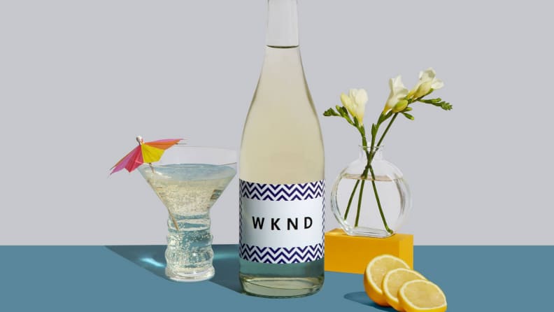 A bottle of white wine surrounded by a wine glass, a vase filled with flowers, and lemon slices.