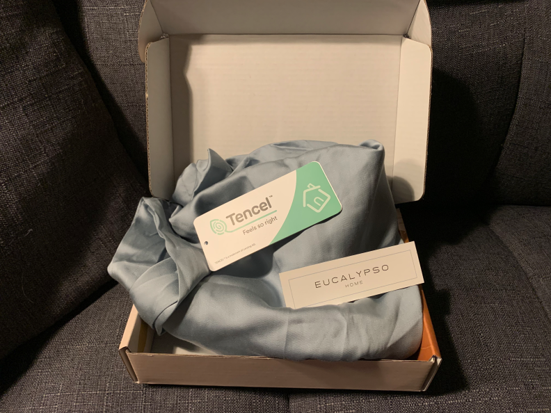 An opened box with a blue pillowcase inside. On top of the pillowcase is a tag that reads, "Tencel / Feels so right" and a tag that reads, "Eucalypso Home."