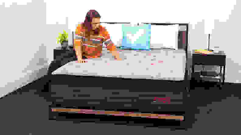A person sitting on the Zoma Boost Hybrid mattress and pressing their hands into the surface.