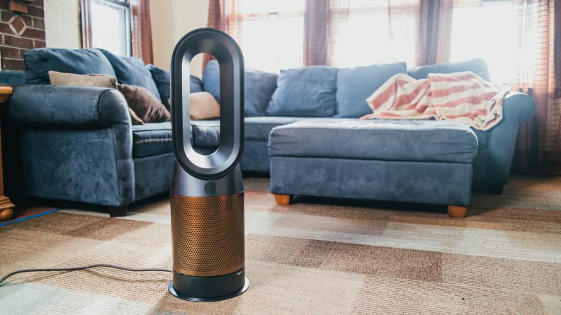 A Dyson air purifier sits at the center of a living room near a blue sectional and matching ottoman.