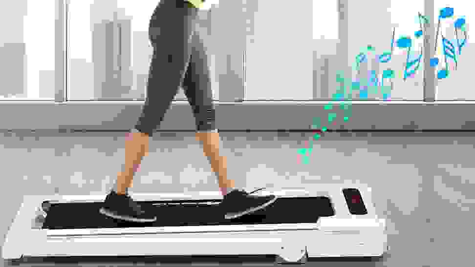 A woman using her treadmill desk to exercise and listen to music.