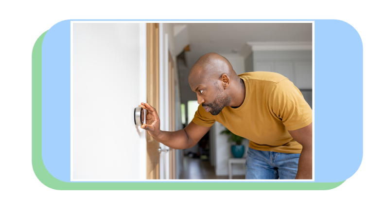 Person hunched over to adjust smart thermostat mounted on wall inside of home.