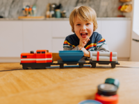 A boy laughing standing next to a toy train