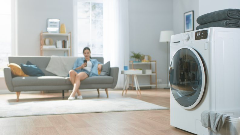 A person sits on a couch waiting for a load of laundry to finish.