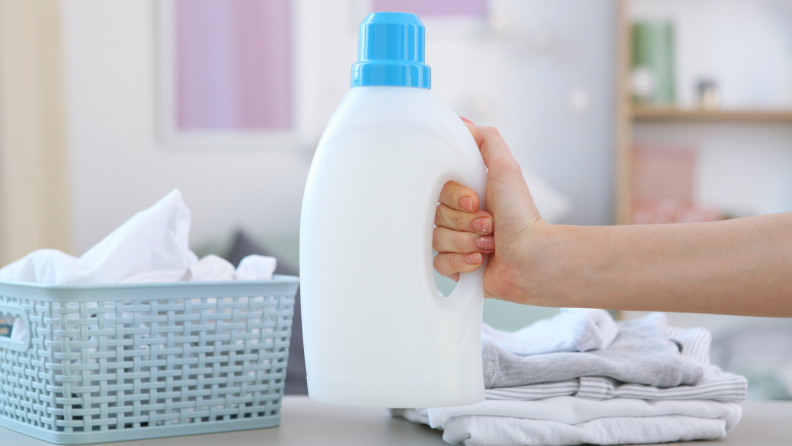 A person holds a bottle of detergent in a laundry room.
