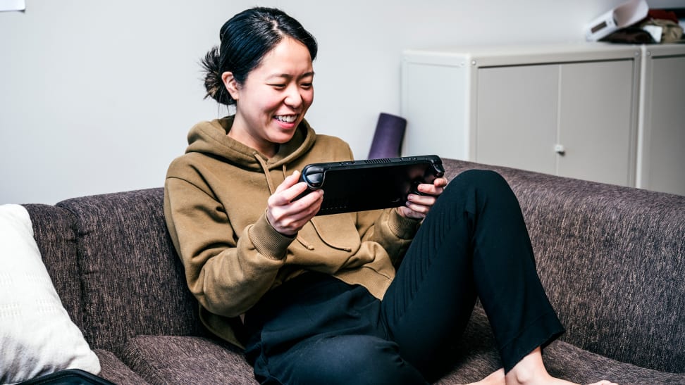 Person seated on couch holding portable gaming device and smiling at screen.