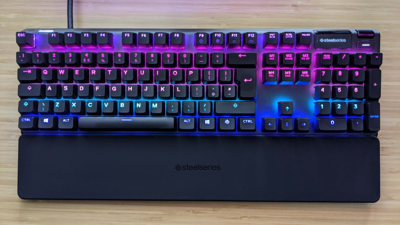 SteelSeries Apex Pro keyboard with multicolor backlights on top of wooden desktop surface.