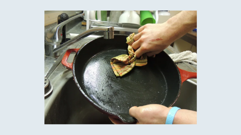 A person wipes a cast-iron pan with a cloth.