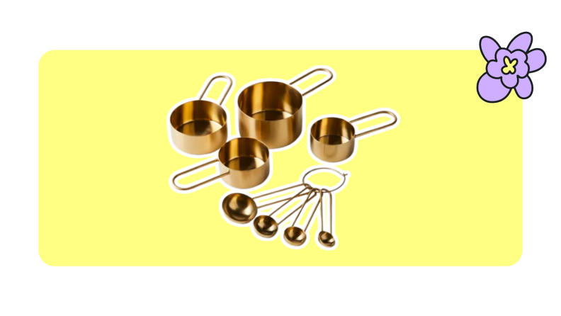 A set of brass Food52 measuring cups and spoons on a yellow background.