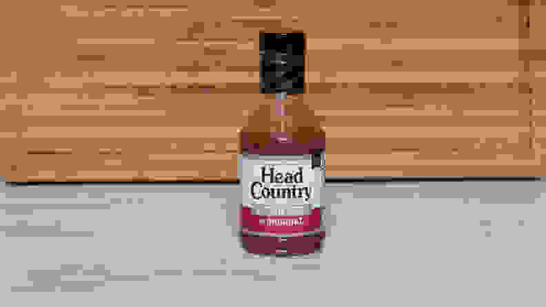 A bottle of Head Country Bar-B-Q Sauce Sugar Free sauce next to a wood cutting board.