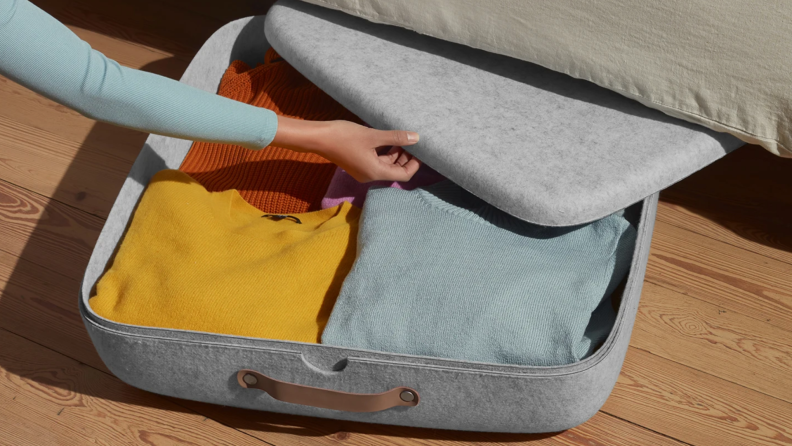 Woman's hand closing up under bed storage container filled with sweaters.