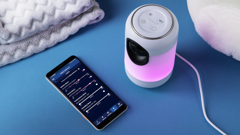 A Yogasleep Ohma baby monitor sitting next to a phone with a screen showing the companion app.