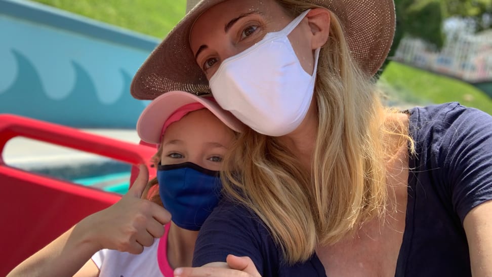 A young girl and a her mom both wearing masks and hats on a Disneyland ride