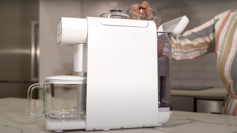 A person is pouring water into the water tank of a ChefWave Milkmade vegan milk maker.