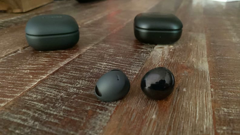 The Samsung Galaxy Buds 2 Pro and Galaxy Buds Pro sit next to one another on a wooden table with their cases in the background.
