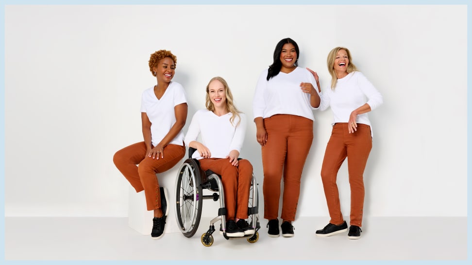Four women, with one sitting in a wheelchair, are all wearing white T-shirts and Adaptive Denim Co. orange jeans.