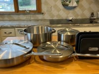 Caraway's stainless steel cookware set sitting on top of wooden island inside of modern kitchen.