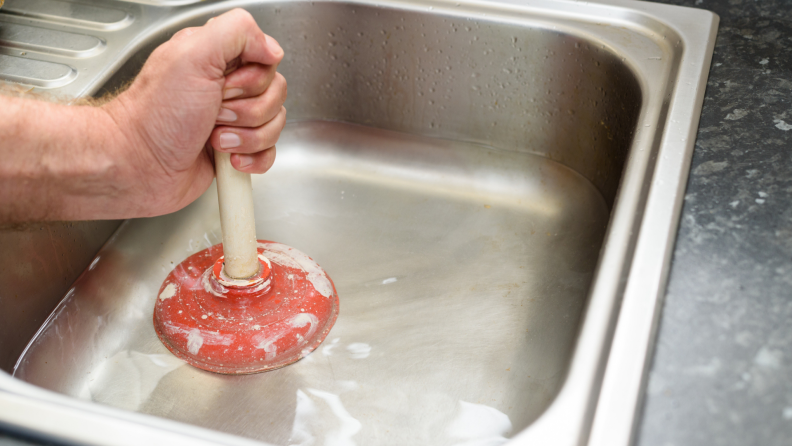 A person plunges a clogged kitchen sink.