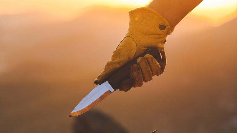 A person wearing gloves holds a knife outside.