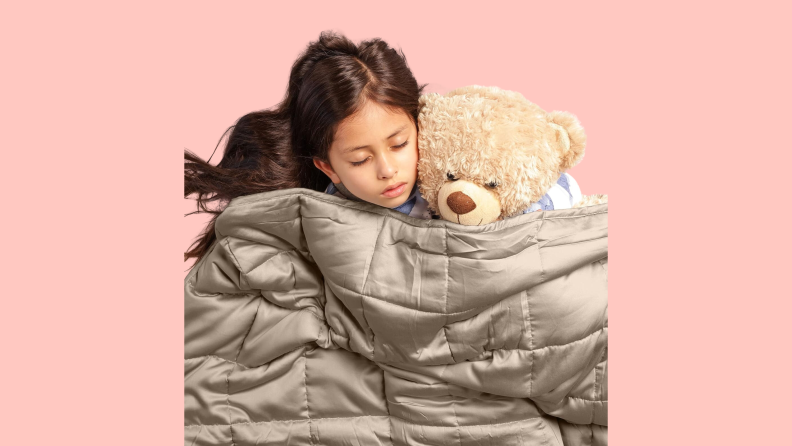 A child sleeping with a teddy bear and a weighted blanket.