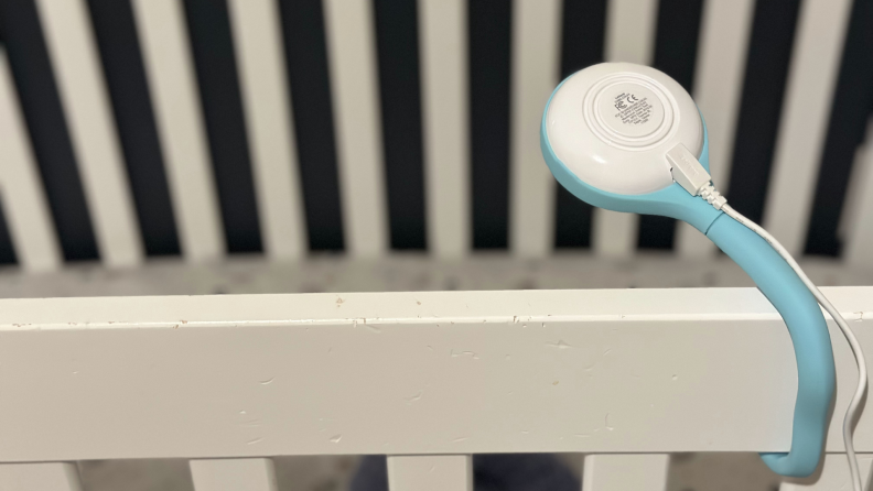 Lollipop Smart Baby Camera in turquoise and white color angled downwards over baby crib with power cord on back half.