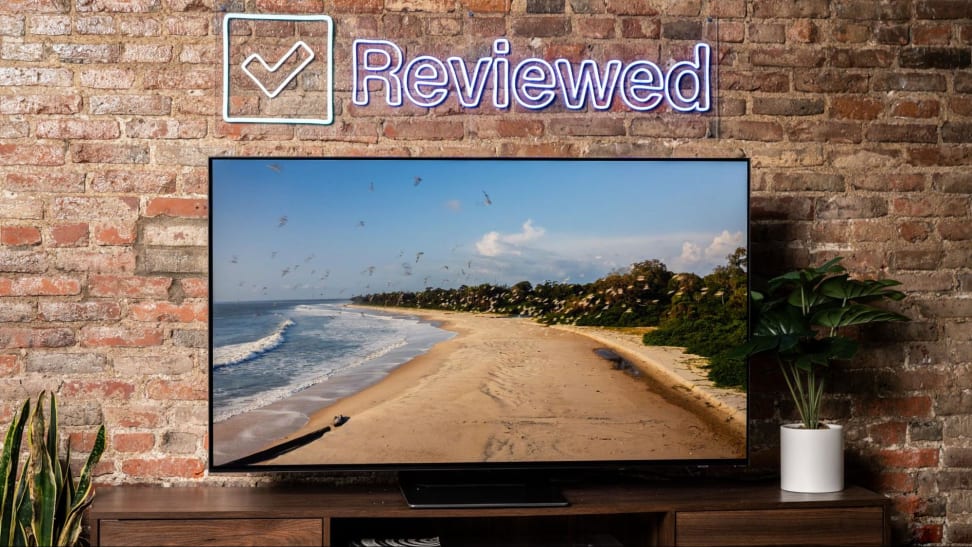 A Samsung S95B QD-OLED television displays an image of a beach in a living room.
